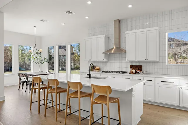 a kitchen with stainless steel appliances granite countertop a stove a refrigerator a sink dishwasher a dining table and chairs with wooden floor