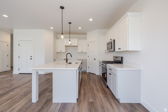 195 West Harmony Rdg Parkway, Unit 601 Mapleton, UT 84664 - Photo 7 of 23 Modern kitchen featuring an island with a built-in sink and matte black faucet, white shaker cabinetry, stainless steel appliances, and wood-finish flooring
