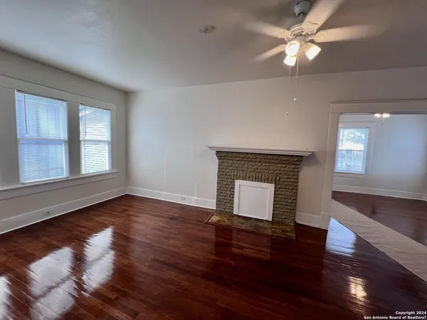a view of an empty room with wooden floor fireplace and a window