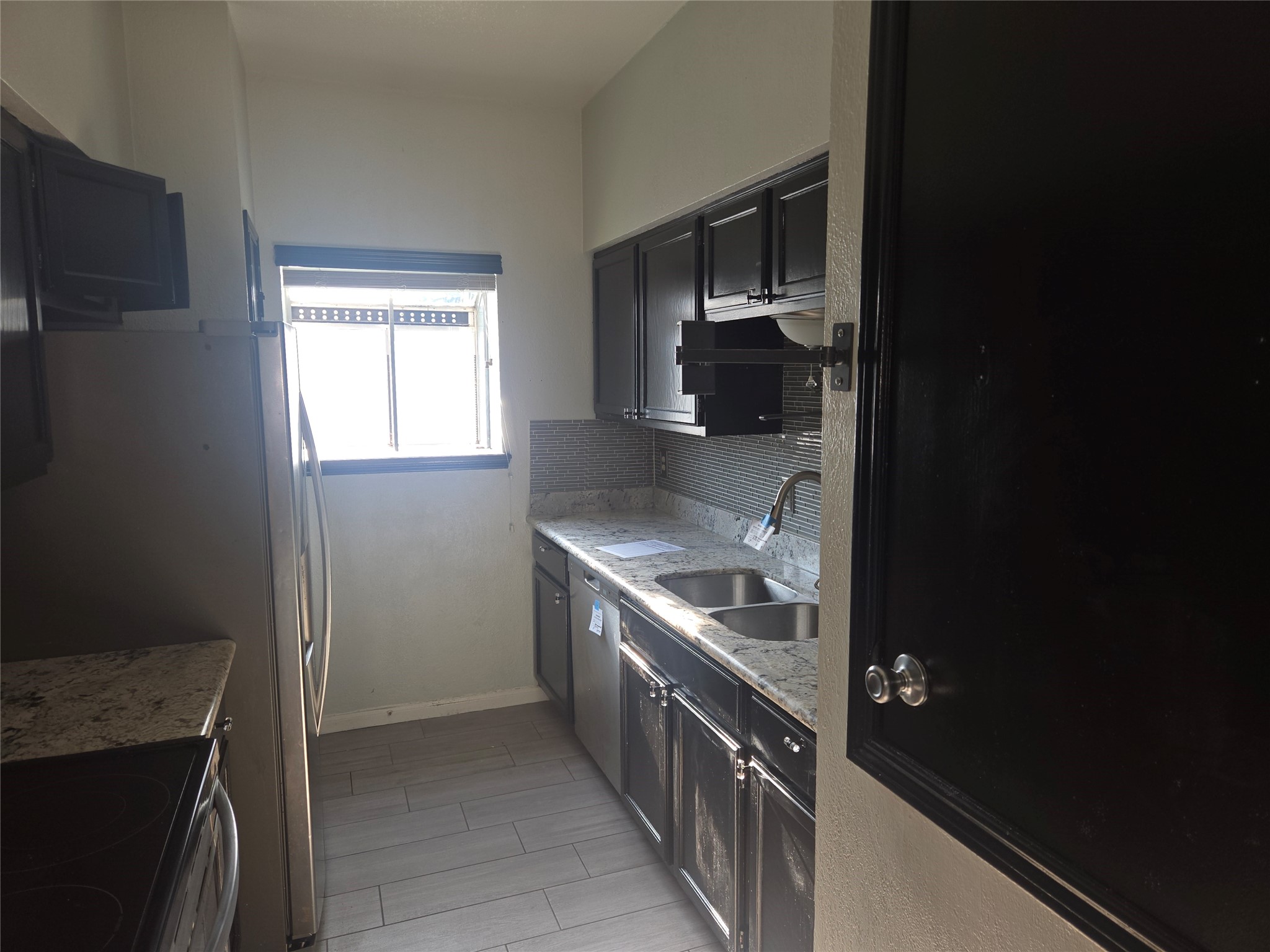 3780 Tanglewilde Street, Unit 501 Houston, TX 77063 - Photo 17 of 26 This kitchen features a galley layout with dark cabinets and stainless steel appliances. It has a modern backsplash, granite countertops, and a window for natural light.