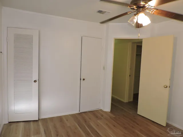 a view of an empty room with wooden floor and a ceiling fan