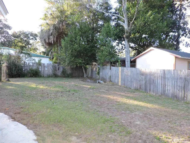 a view of a backyard with large trees and wooden fence