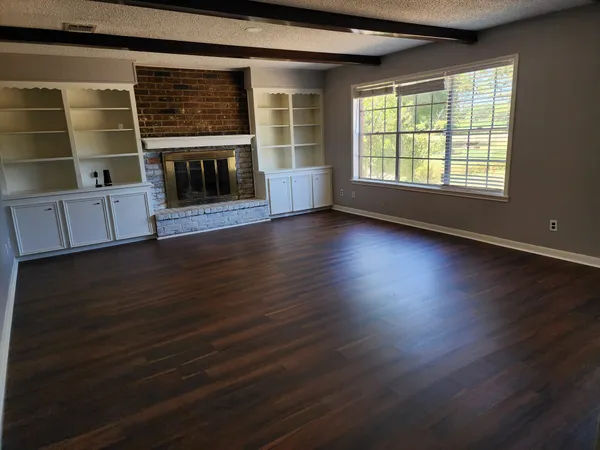 an empty room with wooden floor fireplace and windows