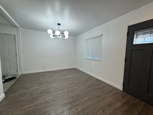 an empty room with wooden floor chandelier and windows