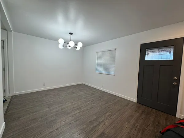 an empty room with wooden floor chandelier and windows