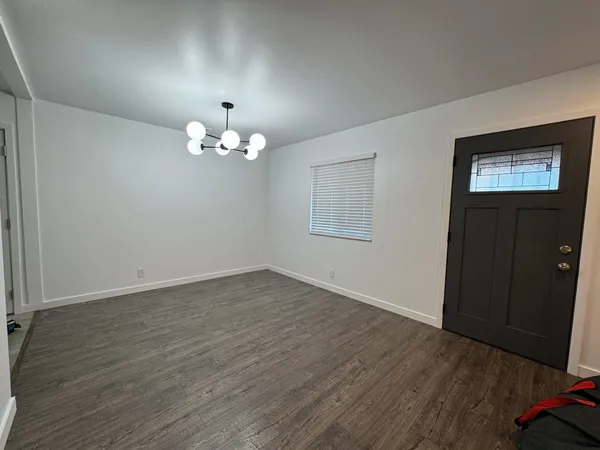 an empty room with wooden floor chandelier and windows