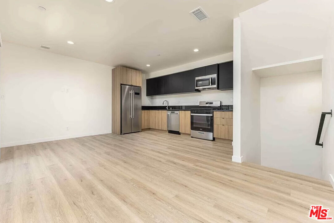 a view of kitchen with stainless steel appliances wooden floor and living room