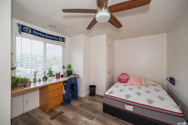 677 300 North, Unit 7 Provo, UT 84606 - Photo 6 of 16 Bright room featuring a wide window with blinds, a built-in desk with three drawers, wood-finish flooring, a ceiling fan, and a white paneled door
