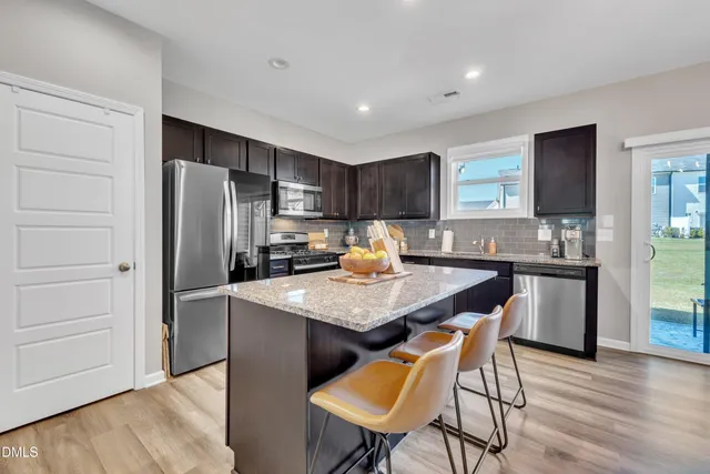 a kitchen with stainless steel appliances granite countertop a refrigerator a stove a sink a dining table and chairs with wooden floor