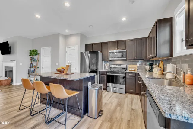 a kitchen with stainless steel appliances granite countertop a stove top oven a sink dishwasher a dining table and chairs with wooden floor