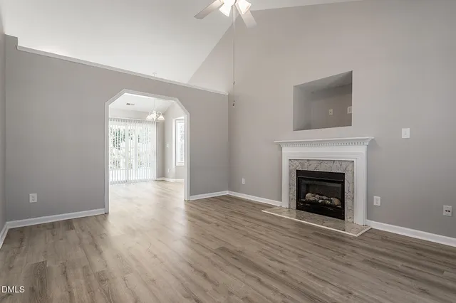 a view of an empty room with wooden floor fireplace and a window