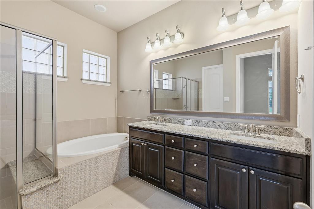 768 Huntingdon Street Coppell, TX 75019 - Photo 11 of 37 Relaxing primary bath with dual sinks, granite countertop, framed mirror, dark cabinetry, soaking tub, separate shower, and soft neutral tile.