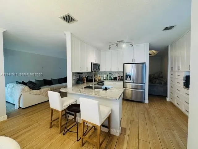 a kitchen with stainless steel appliances granite countertop a sink a stove a refrigerator and white cabinets with wooden floor