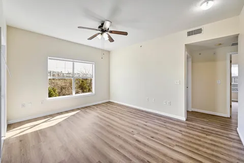 an empty room with wooden floor chandelier fan and windows