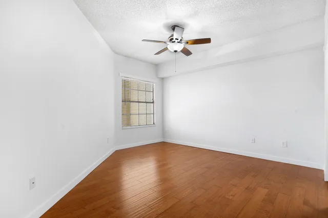 an empty room with wooden floor fan and windows