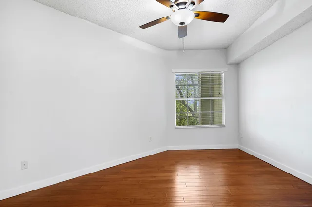 an empty room with wooden floor chandelier fan and windows