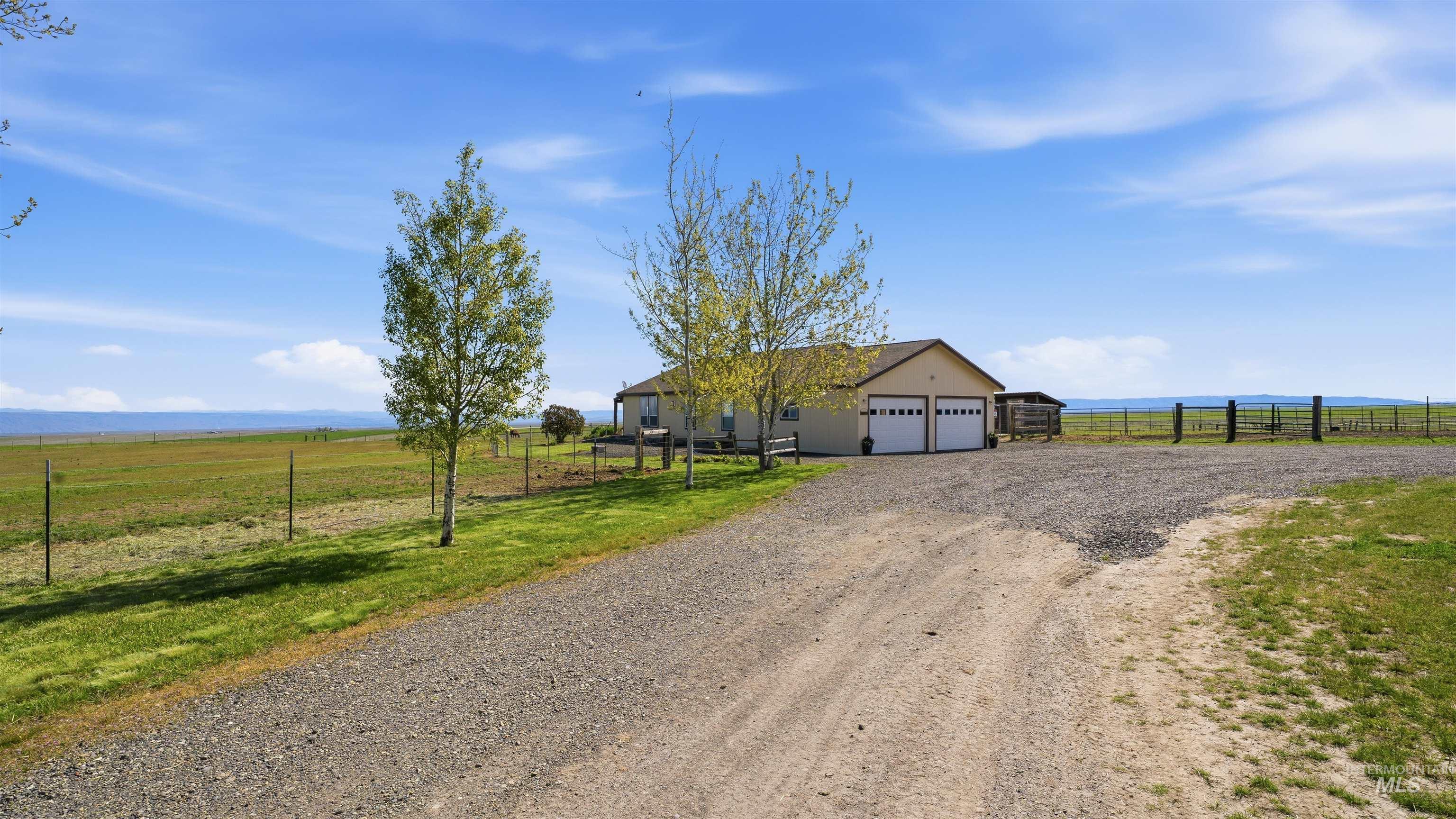 Ranch-style residence featuring a two-car garage with white paneled doors, a gravel driveway, and a large expanse of open land
