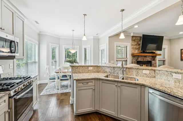 a kitchen with stainless steel appliances granite countertop a stove top oven a sink dishwasher a dining table and chairs with wooden floor