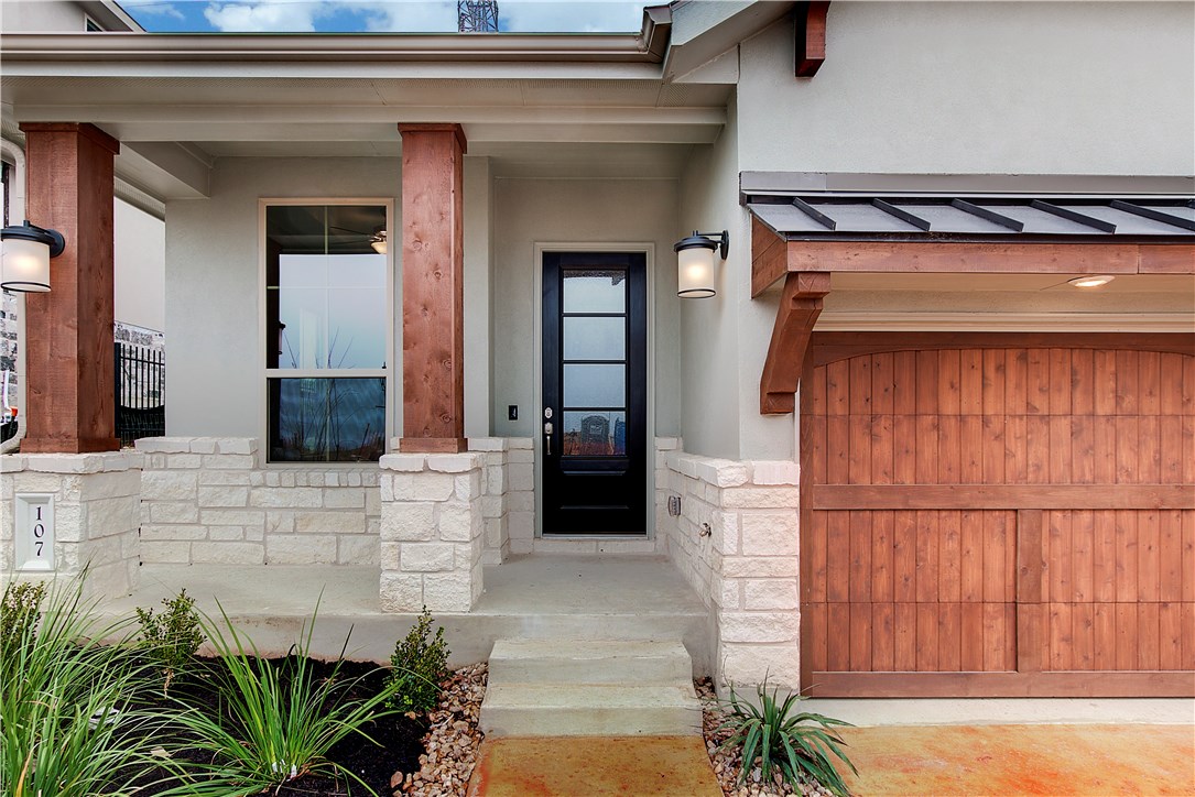 Property entrance with stone siding, stucco siding, covered porch, and a garage