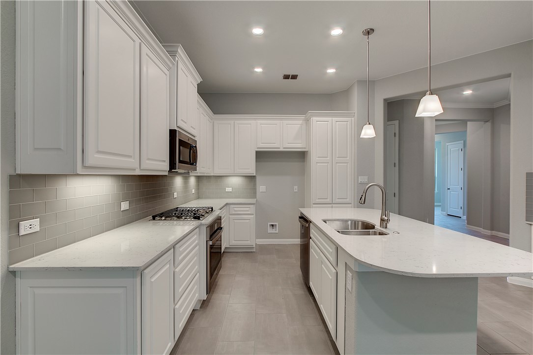 107 Cartwheel Bend Austin, TX 78738 - Photo 5 of 16 Kitchen featuring an island with sink, white cabinetry, light stone counters, and pendant lighting