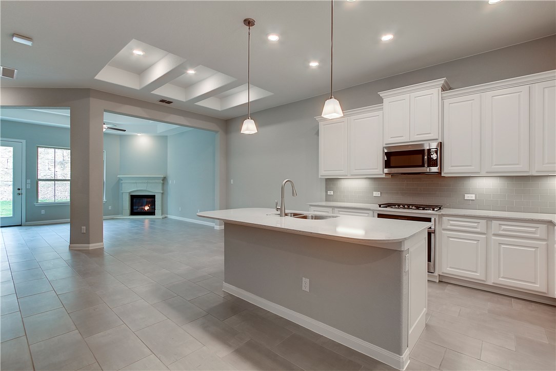 107 Cartwheel Bend Austin, TX 78738 - Photo 16 of 16 Kitchen featuring a glass covered fireplace, stainless steel microwave, a center island with sink, open floor plan, and white cabinets