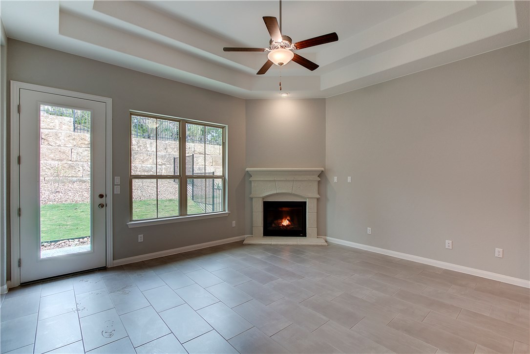 107 Cartwheel Bend Austin, TX 78738 - Photo 7 of 16 Unfurnished living room featuring ceiling fan, a lit fireplace, and a tray ceiling