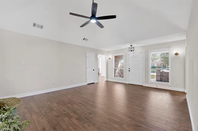 an empty room with wooden floor chandelier fan and windows