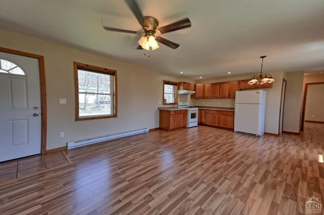 an empty room with wooden floor a ceiling fan and kitchen view