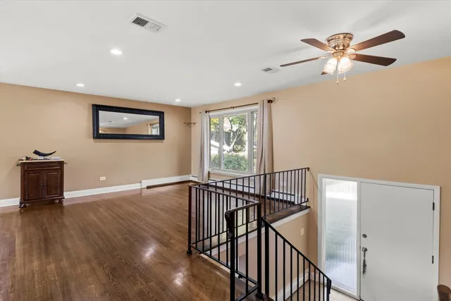 a view of an empty room with wooden floor and a ceiling fan