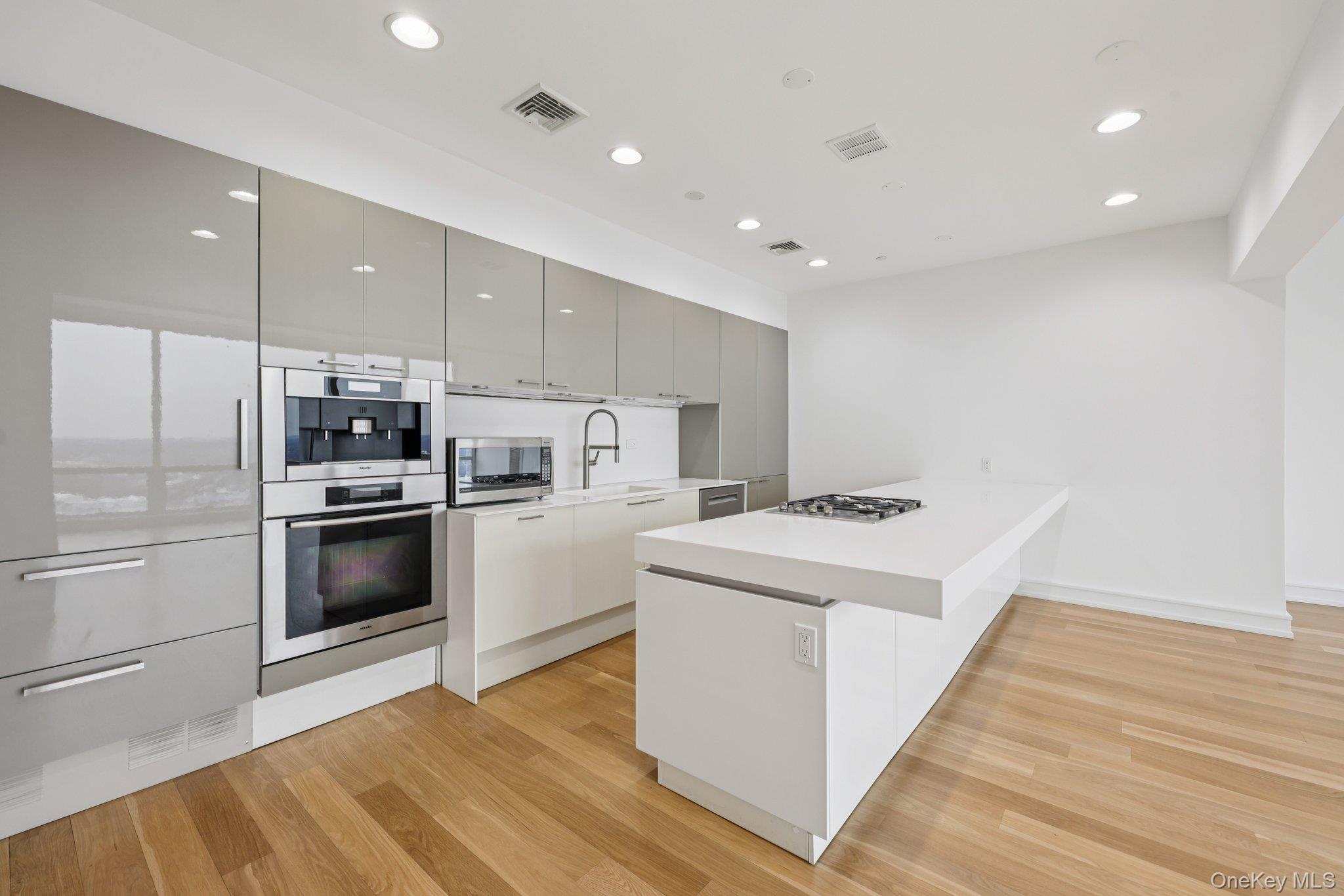 Kitchen with modern cabinets, a peninsula, appliances with stainless steel finishes, light wood-style flooring, and recessed lighting