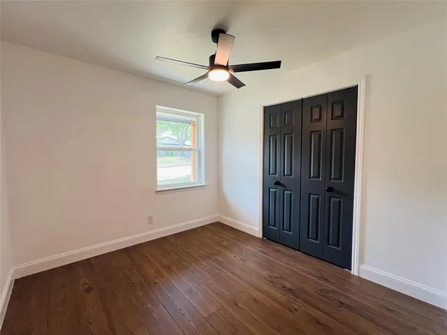 an empty room with wooden floor ceiling fan and windows