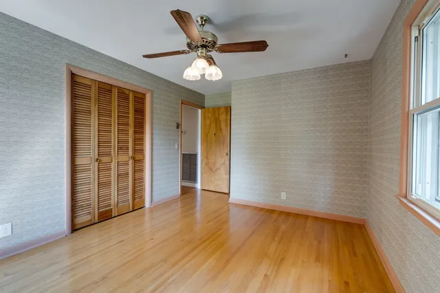 an empty room with wooden floor fan and windows
