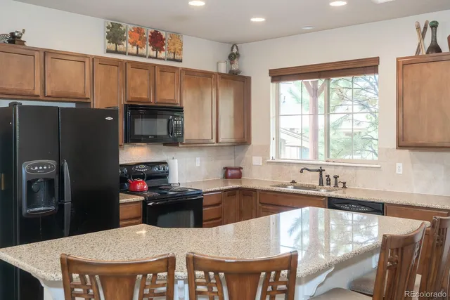 a kitchen with stainless steel appliances granite countertop a stove a refrigerator a sink a dining table and chairs