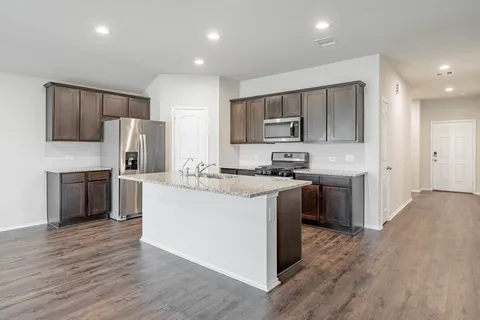 a kitchen with kitchen island granite countertop wooden floors appliances and cabinets