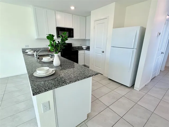 a kitchen with stainless steel appliances granite countertop a refrigerator a sink a microwave a stove and white cabinets