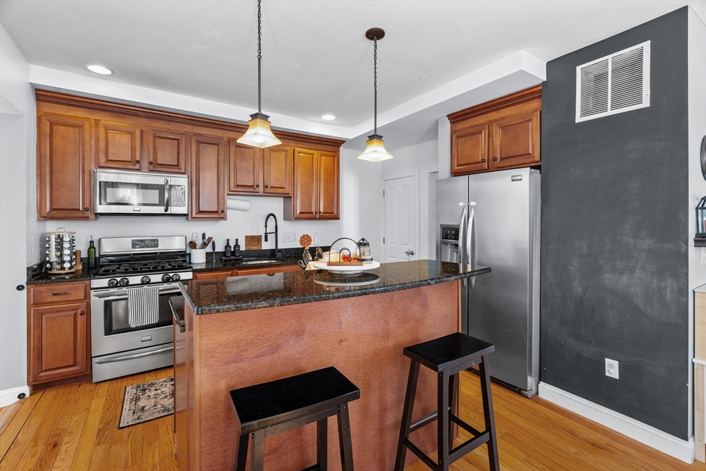 146 South Pleasant Street, Unit 146 Haverhill, MA 01835 - Photo 7 of 28 a kitchen with stainless steel appliances granite countertop a refrigerator a stove a sink dishwasher and a dining table with wooden floor