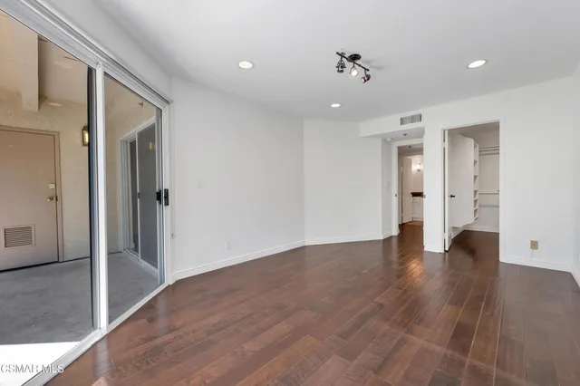 a view of an empty room with wooden floor and a ceiling fan