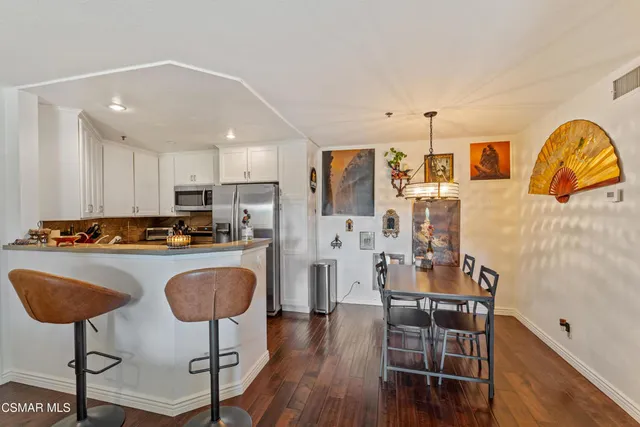 a kitchen with stainless steel appliances granite countertop a stove a refrigerator a kitchen island a dining table and chairs with wooden floor