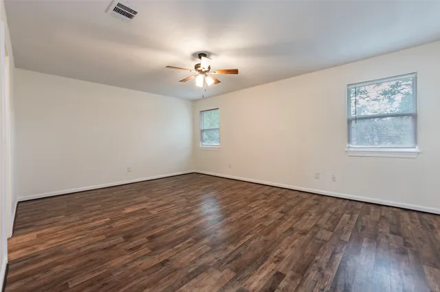 an empty room with wooden floor chandelier fan and windows