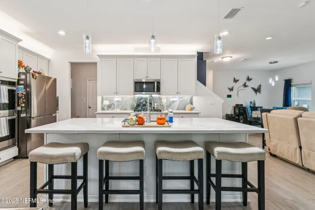 a kitchen with stainless steel appliances granite countertop a dining table chairs refrigerator and microwave