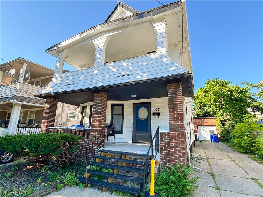 977 Nathaniel Road Cleveland, OH 44110 - Photo 2 of 22 Multi-story residence featuring white siding, a covered front porch with brick columns, and a paved driveway leading to a detached garage