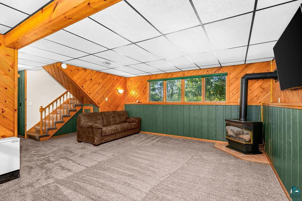 5370 Ugstad Road Hermantown, MN 55811 - Photo 8 of 68 Wood paneling, wood-burning stove, wall-mounted television, windows, and exposed ceiling beams