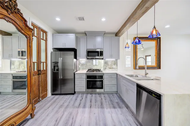 a kitchen with stainless steel appliances a stove a sink dishwasher a refrigerator and a oven with wooden floor