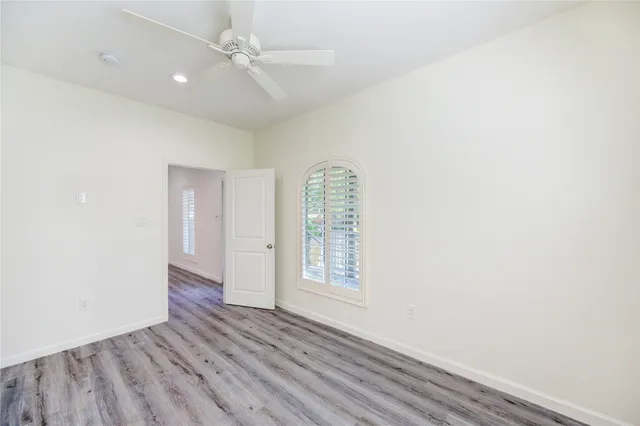 an empty room with wooden floor chandelier fan and windows