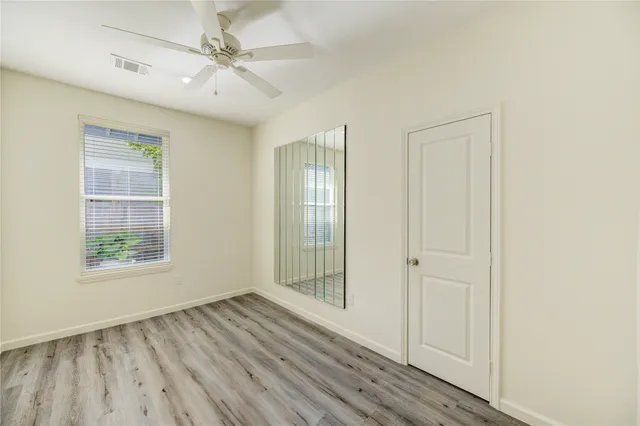 an empty room with wooden floor ceiling fan and windows