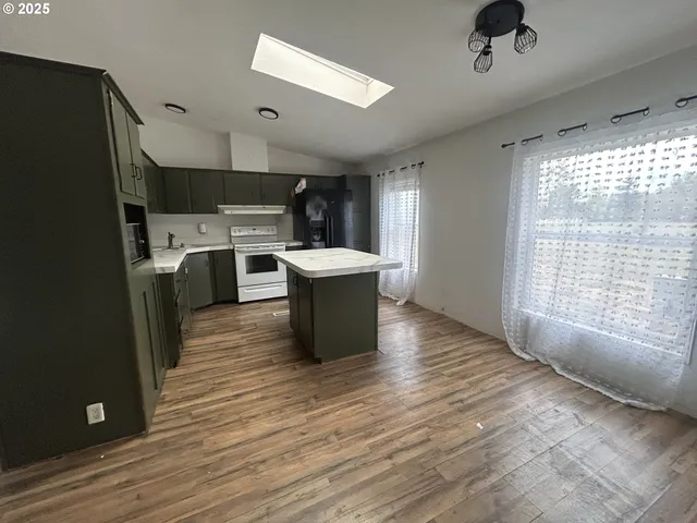 a living room with stainless steel appliances a kitchen island hardwood floor and a large window