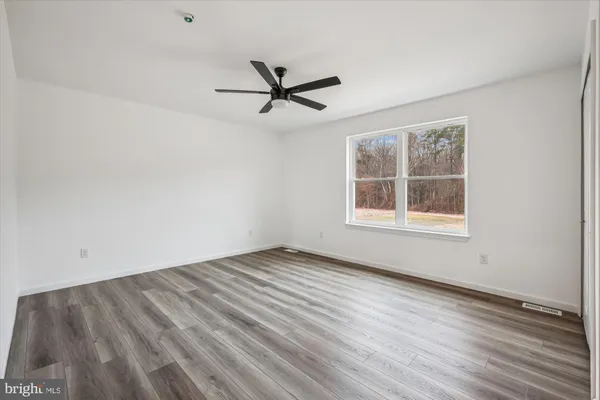 a view of an empty room with wooden floor and a ceiling fan