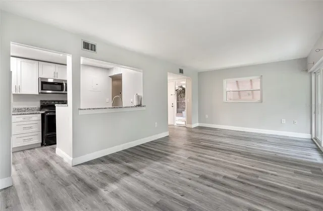 an empty room with wooden floor and a kitchen