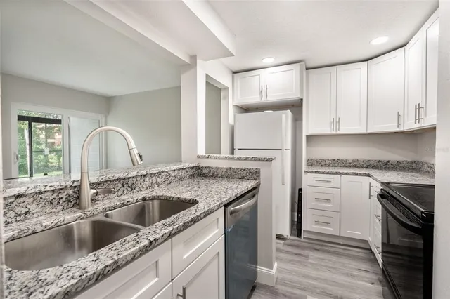 a kitchen with granite countertop a sink dishwasher a stove and a refrigerator with wooden floor