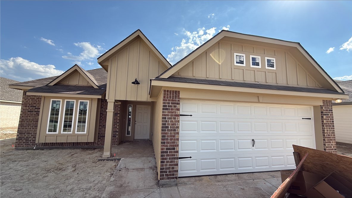 View of front facade with brick siding, a shingled roof, a garage, and board and batten siding
